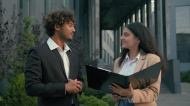 Şehirdeki iki iş kadını Arap kadın işkadını elinde dosya kağıtları tutan stajyer Hintli işadamı yatırımcı lideriyle el sıkışarak gülümseyerek el sıkışma anlaşması yapıyor.