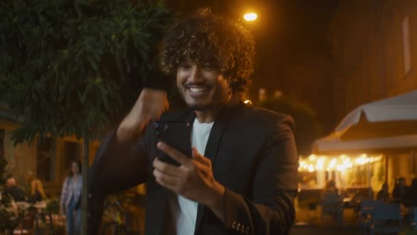 インドのアラビアのラテン系アメリカ人男性興奮男性携帯電話の笑顔を達成幸せな運の男の勝利を楽しむスマートフォン楽しいチャンピオンの幸運のお祝い都市外勝利は驚きました — ストック動画