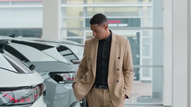 アフリカ系アメリカ人男性男性男性カスタマーバイヤー 夢見る 自動車ショールームペンシブクライアントビジネスマン ディーラーで歩く 自動車クロスオーバー新しい現代電気自動車を選択することを考えます — ストック動画