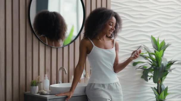 非裔美国人快乐微笑的女人用手机浏览聊天智能手机女孩电话社交媒体在浴室美容程序中发送短信网上购物网上冲浪应用 — 图库视频影像