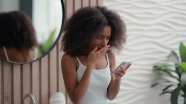 Afro-Amerikalı güzel bir kadın sabah banyosunda günlük güzellik derisi saç bakımı duygusal hayal kırıklığına uğramış üzgün üzgün bir kız kötü haber cep telefonu problemini okuyor çok kötü bir SMS akıllı telefon hatası