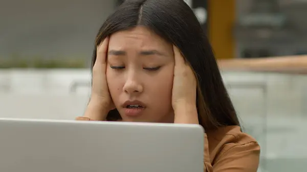 Exhausted overworked Asian woman girl student studying online work on laptop in office hold head headache tired chinese korean female employee businesswoman upset job failure despair fatigue burnout