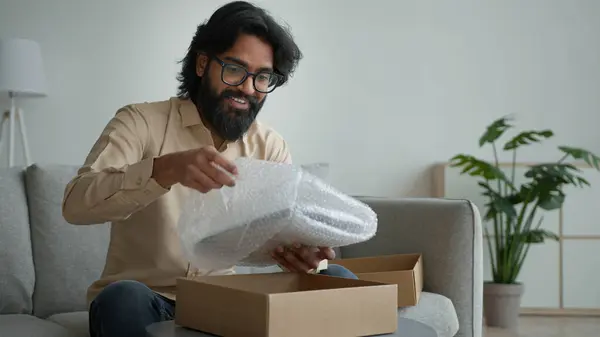 快乐的男性顾客客户消费者阿拉伯印度男人戴眼镜打开纸板箱在家里打开包装网上购物定单购买包裹收件送礼拆箱包裹 — 图库照片