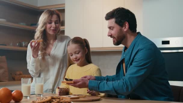 快乐的白种人父母带着孩子的女儿在厨房一起准备早餐享受有机食品递送吃巧克力三明治妈妈 爸爸小女孩 — 图库视频影像