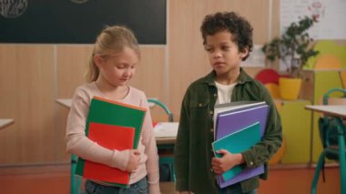 İki mutlu yaramaz öğrenci çeşitli etnik çeşitlilikteki çocuklar Afrikalı Amerikalı erkek ve Kafkas kız sınıf arkadaşları eğlenceli eğleniyorlar birbirlerini itip kakıyorlar okulda alay eden dilleri gösteriyorlar.