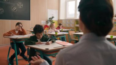 Geçmişe dönüp baktığımızda, tanınmayan bayan öğretmen, okul dersinde öğretmen, çocuklara ilköğretim öğretiyor, çocuklara ilköğretim öğretiyor, çocuklarla konuşuyor, oğlanlarla konuşuyor, öğretmenlik yapıyor, okul çeşitliliğini anlatıyor.