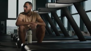 Yorgun Afrika kökenli Amerikalı sporcu fitness spor salonunda dinleniyor yorgun düşmüş koşu bandında yorgun ve susamış bir şekilde koşan terli adam dinleniyor su proteini şişesi içiyor.