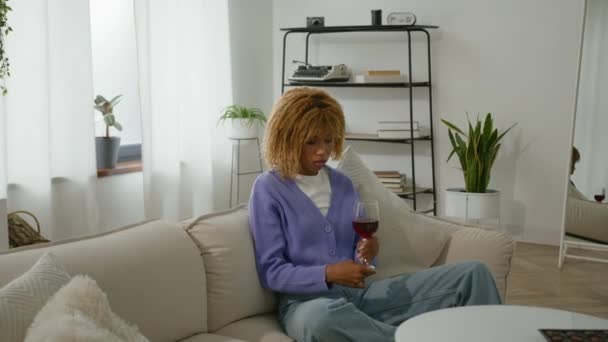 忧心忡忡忧心忡忡忧心忡忡孤独的非裔美籍女子在沙发沙发上孤独的女性酗酒成瘾症健康问题想把杯子放在桌上 — 图库视频影像