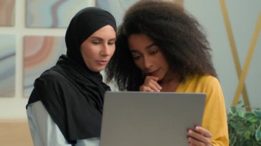 Mutlu gülümseyen iş kadınları, çok ırklı iş kadınları, iş arkadaşları, internet projelerini tartışırlar. Laptop Arap Müslüman kız tesettüre girmiş, tesettüre girmiş, Afrikalı Amerikalı kadın müşteriye danışıyorlar.