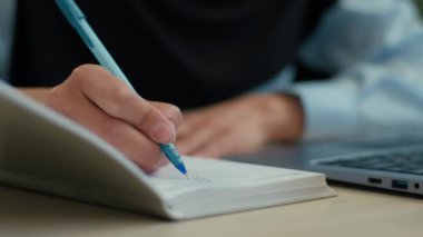 Not defterine kadın el yazısını kapat tanınmayan iş kadını müslüman kadın tesettüre girmiş, tesettüre girmiş, tesettür öğrencisi, not yazıyor iş evrakları, ofis bilgisayarında dizüstü bilgisayarla finans bütçesi.