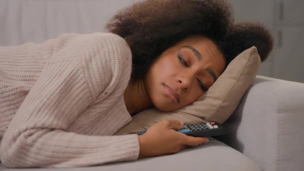 アフリカ系アメリカ人の疲れた女の子一人でソファーの家に横たわるリモートコントロールスイッチチャンネルを保持する 退屈な週末のテレビを見る 孤独な退屈なリラックス ソファで悲しみの落ち込んだ不満の女性の非アクティブな無関心 — ストック動画