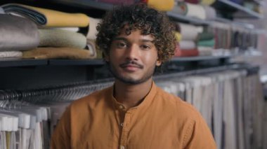 Arap Hindistanlı etnik erkek müşteri satıcısı moda tasarımcısı tekstil dükkanında moda tasarımcısı mutlu erkek işadamı elbise dikme elbisesi giydirme kıyafetleri giydirme kameraya gülümseyen adam