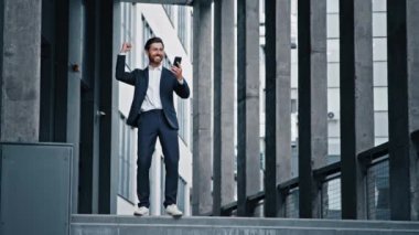 Heyecanlı beyaz adam mutlu iş adamı SMS mesajı alıyor cep telefonundan iyi haberler okuyor ofis binasının yakınındaki erkek kazananı kutluyor zaferi online zaferle kutluyor