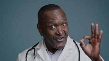 Mutlu Afro-Amerikan portresi gülümseyen erkek doktor, doktor, cerrah, profesyonel doktor, stüdyo mavi arka plan çalışanı.