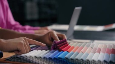 Kapalı ellerde moda tasarımcısı kumaş kumaş koleksiyonu seçiyor. Kırpılmış çekim kimliği belirsiz adam dizayn için malzeme rengi seçiyor. Kadın dizüstü bilgisayar yazarken atölyede elbise dikiyor.
