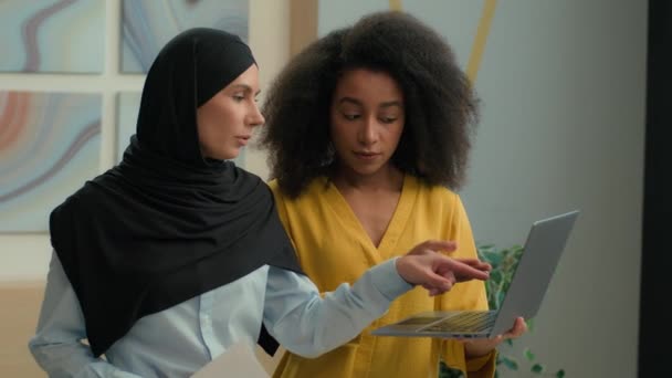 2人の多様な女性 多様な女の子同僚 ビジネスウーマン 話し合い オフィスでラップトップ上のビジネスプロジェクトについて アフリカ系アメリカ人のメンター コンサルティング ヒジャブでアラビアのイスラム教徒の女性を教える — ストック動画