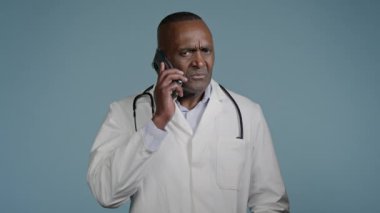Kafası karışmış üzgün Afrikalı Amerikalı doktor cep telefonundan konuşuyor. Kötü haber alıyor. Düşünceli erkek doktor hasta telefonuna cevap veriyor.