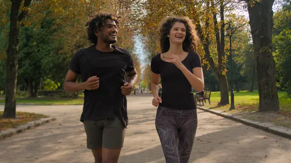 Happy multiracial runners healthy sportsman and sportswoman running outside workout together fitness couple laughing jogging sport activity Arabian man and Caucasian woman jog run in autumn city park