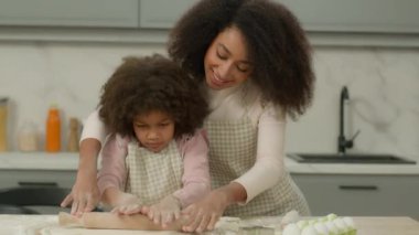 Mutlu Afro-Amerikan ailesi ev mutfağında anne, tatlı bir kız çocuğuna hamur yoğurmayı öğretiyor. Yuvarlanan iğne, anneye kurabiye pişirmede yardımcı oluyor.