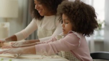Yiyecek teslimatı eko ürünleri un süpermarketi mutlu Afrikalı Amerikalı anne küçük kız çocuğuna mutfakta lobutlarla hamuru düzleştirmeyi ve pizza turtası pişirmeyi öğretiyor.