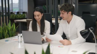 Beyaz kadın ve erkek birlikte çalışıyor kağıtlar ve dizüstü bilgisayarla gülümsüyor gülerek mutlu mesut evrak işleriyle gülüyor ofis iş arkadaşlarıyla gülüyor iş kadını ve iş kadını şakadan keyif alıyorlar.