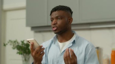 Ciddi Afrikalı erkek etnik adam sesli mesaj kaydediyor. Sesli mesaj, konuşma, cep telefonu hoparlörü. Sosyal medya, akıllı telefon, evde yüksek sesli cep telefonu mikrofonu.