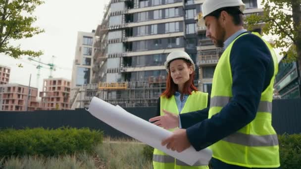 2人の建築家 都市建設労働者 コーカサス同僚 安全帽子と反射ベストのパートナー 都市ブループリントビルダーエンジニア 女性と男性 建築計画について話し合う — ストック動画