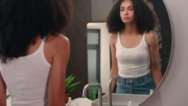 朝の美のプロシージャ不健康な悲しいアフリカ系アメリカ人女性の散歩は 鏡の反射チェック肌の顔面に触れる顔の問題スキンケア悪い複雑なアクネのしわを見て浴室に来ます — ストック動画