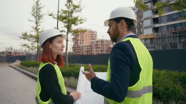 ブループリントの情報をチェックする2人の請負業者の市民エンジニアがチームワークを議論し 都市開発計画の共同建設労働者を計画する都市ビルディングプロジェクトマネージャーを指摘 — ストック動画