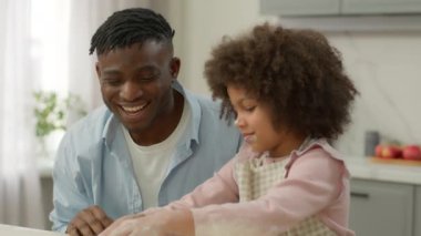 Afro-Amerikalı mutlu baba, un hamuruyla yemek yapan küçük kız çocuğu destekliyor. Babası alkışlıyor. Etnik aileyi alkışlıyor.