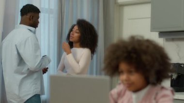 Afrika kökenli Amerikalı çift, mutlu erkek, mutfakta mutlu aile, karı koca konuşuyor, bulanık küçük kız öğrenci, e-öğrenim öğrenimi görüyor, bilgisayar oyunu oynayarak bilgisayar oyunu oynuyor.