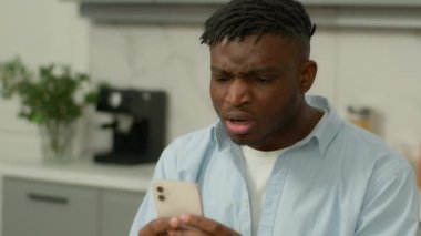 Stresli Afro-Amerikalı etnik adam cep telefonuyla ilgili kötü haberleri evde okudu sorun bildirme problemini kaybetti akıllı telefonu kaybetti kafası karışmış erkek cep telefonu stres hatasından şikayetçi oldu