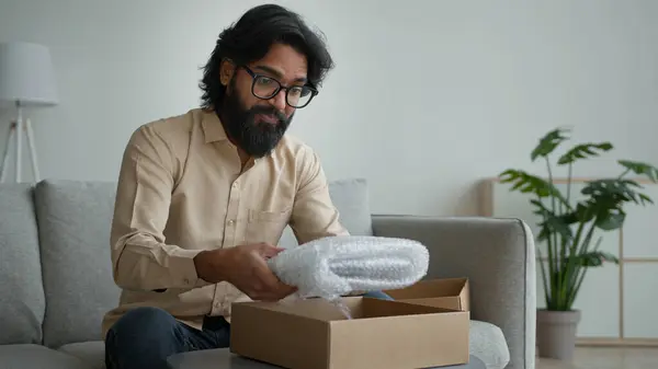 快乐的男性顾客客户消费者阿拉伯印度男人戴眼镜打开纸板箱在家里打开包装网上购物定单购买包裹收件送礼拆箱包裹 — 图库照片