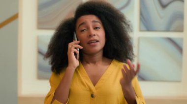 Memnun olmayan sinirli etnik iş kadını Afrikalı Amerikalı iş kadını ofiste cep telefonuyla konuşuyor. Kadın girişimci işveren hoşnutsuz olduğunu savunan akıllı telefon konuşmasını arıyor.