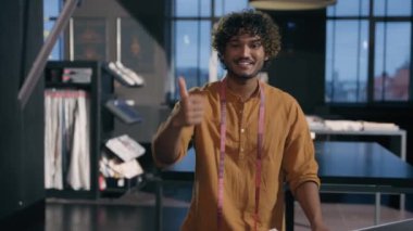 Arap Hindistanlı etnik adam neşeli moda tasarımcısı terzi terzi erkek giyim tasarımcısı küçük işletme sahibi gülümseyerek atölye tekstil dükkanına iyi bir jest yapıyor.