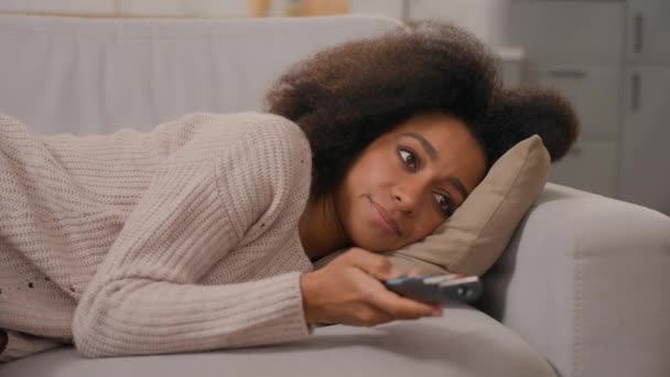 退屈な不満 アフリカ系アメリカ人女性 孤独な若い少女 怠惰な家庭主婦 ソファーに横たわる女性 テレビ チャンネル プログラムを検索 リモート コントロール — ストック動画
