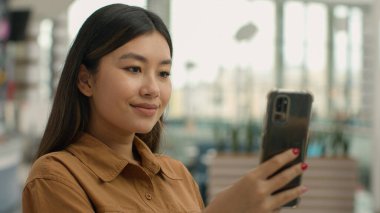 Gülümseyen Asyalı Çinli Japon kadın portresi çok ırklı kız iş kadını sosyal medya akıllı telefon ekranı okuyup Koreli etnik bayan öğrenci sohbeti mesajını cep telefonuyla okuyun.