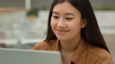 Gülümseyen Asyalı iş kadını Çinli Koreli çok ırklı Japon kız öğrenci uzaktan kumandayla çalışıyor kadın çalışan girişimci yönetici ofiste internet teknolojisine göz atıyor.