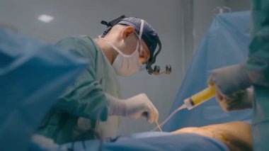 Cerrah doktor doktor karın cerrahisi ameliyatı estetik ameliyat, liposuction prosedürü hemşireler hastane sağlık hizmetlerinde anestezi enjeksiyonu yapıyor.