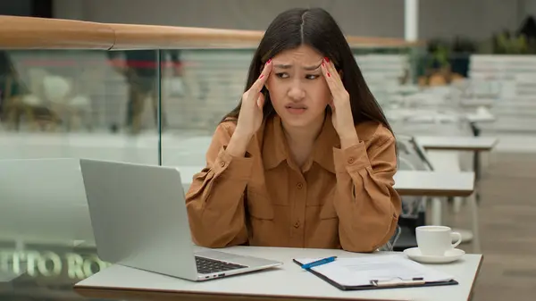 疲れたアジア人の女性がノートパソコンの書類作成の問題でカフェで働くビジネスの難しさ病気不健康な中国人の韓国人のビジネス女性は痛みを伴う頭の頭痛片頭痛が痛い緊張過労を被る — ストック写真