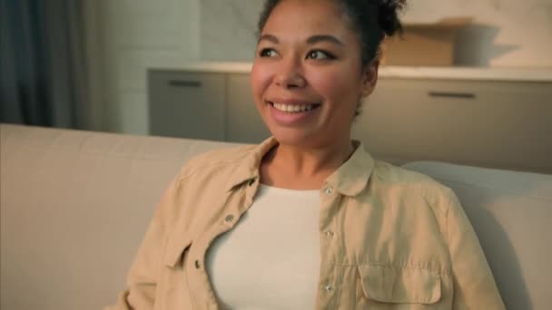 快乐轻松的非洲裔美国女性房主快乐快乐的租房子的女孩坐在沙发上放松享受新房搬迁的快乐 — 图库视频影像