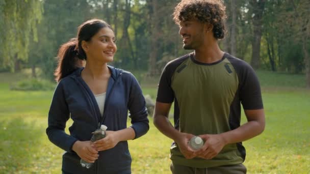 两名体育人士笑着说着拿着水瓶笑着邀请参加运动男性印度女性阿拉伯朋友公园里的男性伴侣邀请受欢迎的健身适合城市的动机 — 图库视频影像