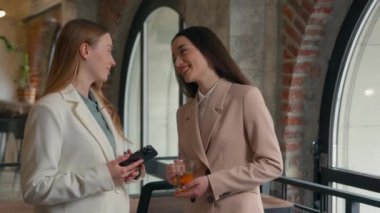 İki mutlu gülümseyen Kafkasyalı kadın ofis çalışanları iş kadınları iş kadınları iş arkadaşları iş konuşmalar sohbet konuşmalar haberler çay fincanları cep telefonu kahkahaları arkadaşlık