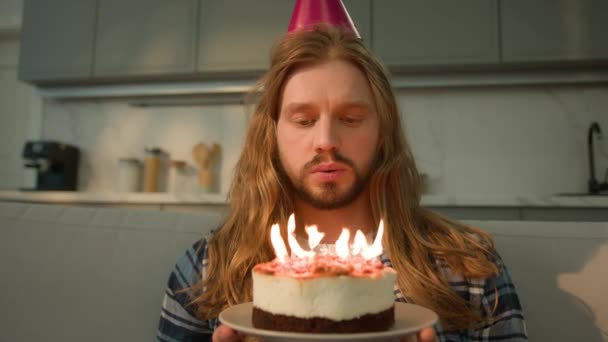 ひとり悲しい動揺 自宅のケーキを吹き飛ばすキャンドルを吹くホールデーケーキの男の1人のコーカサス人の男の欲求が落ち込んだ孤独のお祝いお祝い帽子の絶望が失望した移民 — ストック動画