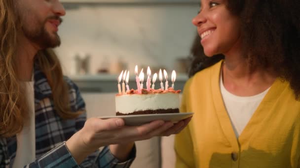 多民族カップル多様な多様性の人々は アフリカ系アメリカ人の誕生日女性ガールフレンドのためにケーキを保持している白人男性ボーイフレンドと結婚しました キャンドルを吹き飛ばしたい 自宅でお祝い — ストック動画