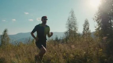 Atletik Kafkasyalı erkek sporcu erkek spor giyim gözlüklü koşucu vadi yürüyüşü yapıyor dağlara tırmanıyor açık havada yeşil tepe tırmanıyor macera macerası yapıyor sağlıklı yaşam tarzı egzersizleri yapıyor.