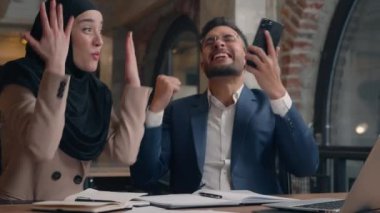 Mutlu, şaşkın, çok ırklı kadın, kazanan iş ortakları, tesettürlü Müslüman iş kadını, cep telefonu başarısı, iyi haber.