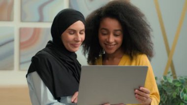Neşeli iş adamları, Afrikalı Amerikalı işveren Arap müslüman islami yönetici tesettürcü çok ırklı kadın meslektaşları birlikte çalışan mutlu kadın iş kadınları dizüstü bilgisayar projesiyle gülümsüyor.