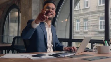 Şirketin iş yerinde dizüstü bilgisayarda çalışan Hintli iş adamı yöneticisi CEO mutlu Arap erkek işadamı kamerayı işaret ediyor.