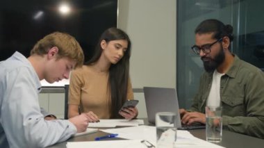Çeşitli Hintli erkekler, iş adamları, beyaz kadın iş adamları, iş ortakları, iş arkadaşları, dizüstü bilgisayarlı cep telefonu cihazları, ofis şirketindeki şirket projelerini analiz ediyorlar.
